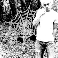 a young man standing in the woods with a spider web